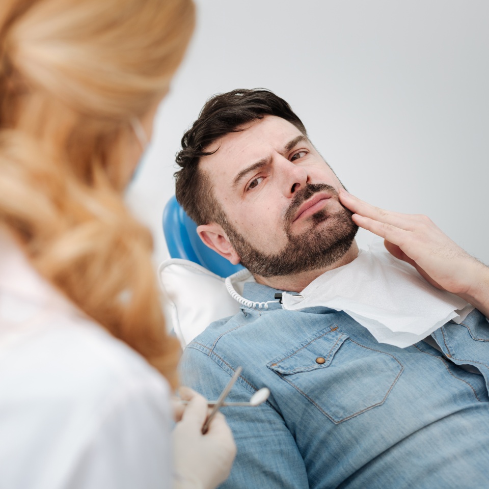 No puedo soportarlo más. Hombre apuesto y preocupado hablando con un doctor sobre sus inquietudes mientras le visita regularmente y está sentado en la silla del dentista.