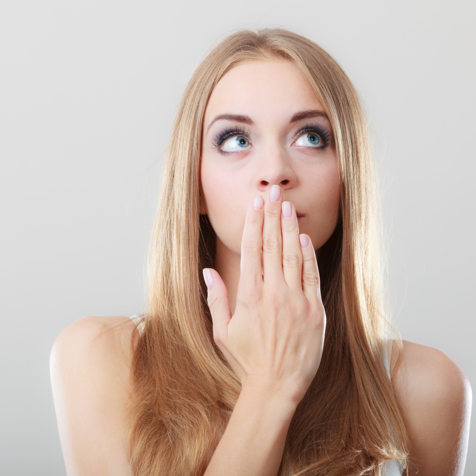 Young amazed woman covering her mouth with hand on gray