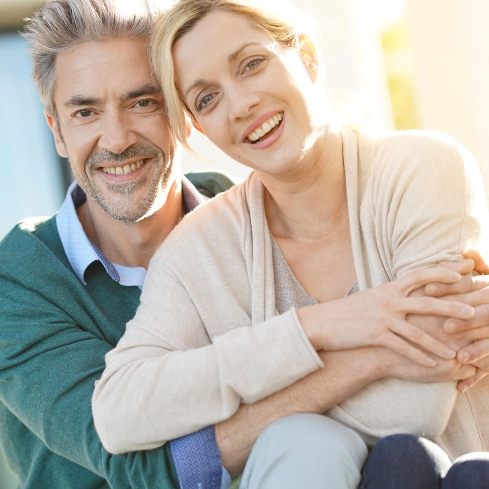 Alegre pareja de mediana edad sentada frente a una casa nueva.
