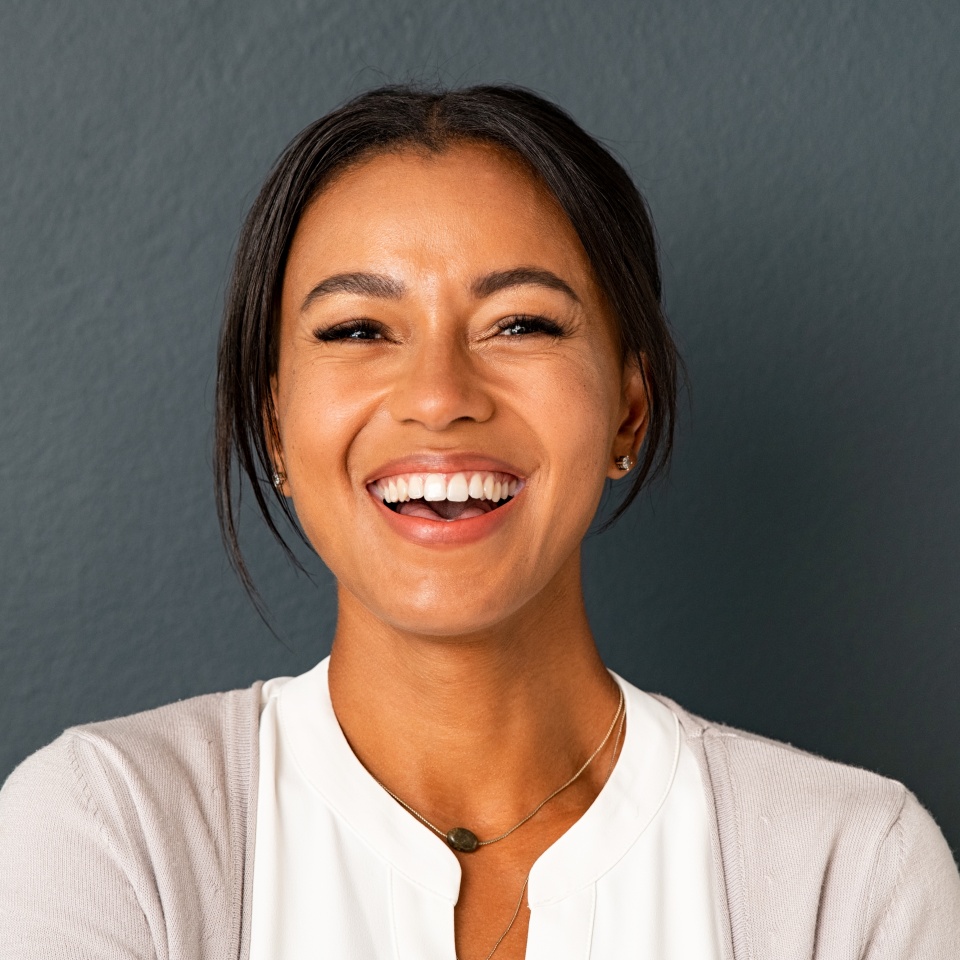 Primer plano del rostro de una mujer hermosa de mediana edad mirando a la cámara con una gran carcajada. Mujer hispana de mediana edad de pie aislada contra una pared gris mientras se divierte. Retrato de una mujer india sonriente riendo.  