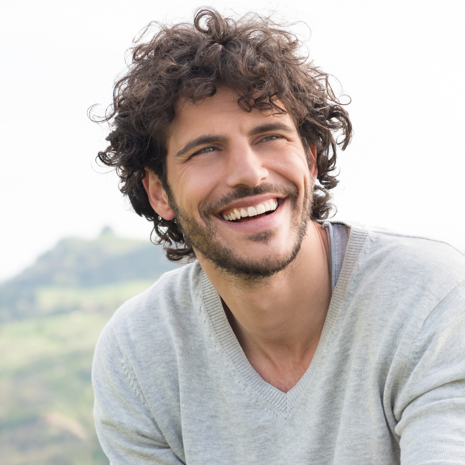 Retrato de un hombre joven y apuesto sonriendo al aire libre.