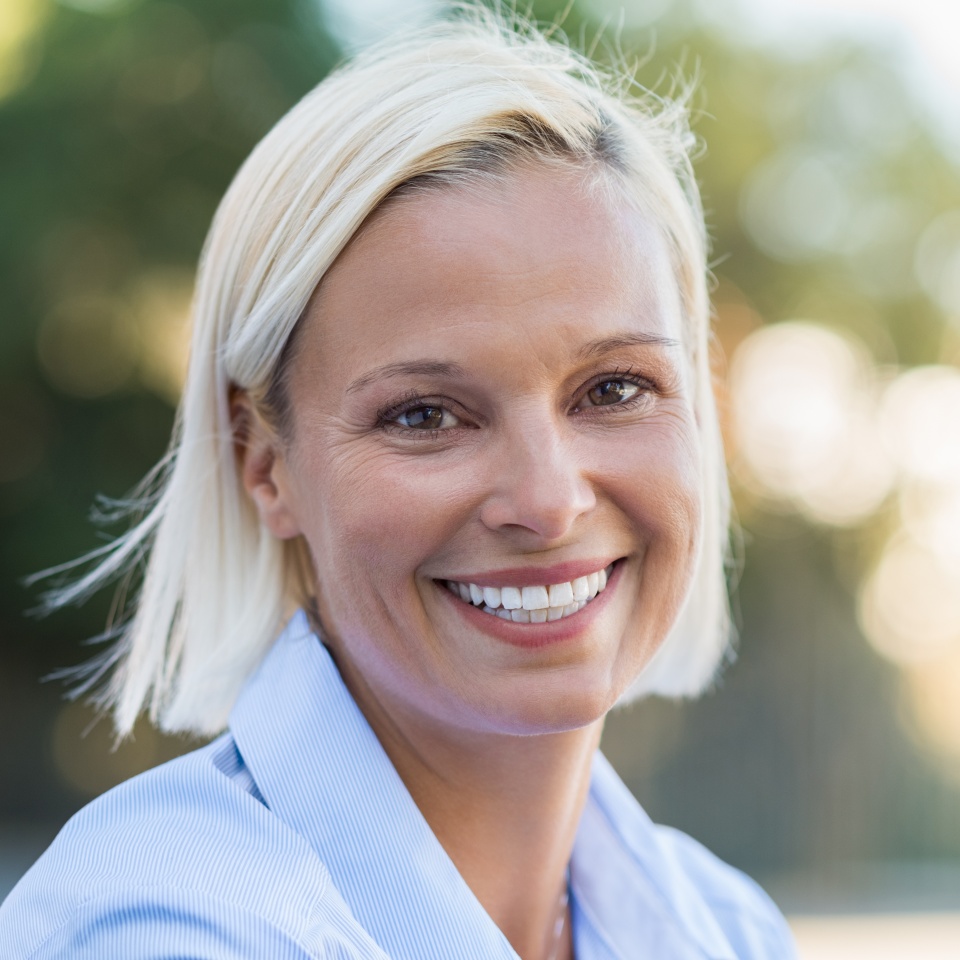 Retrato de mujer madura sonriendo y mirando a la cámara al aire libre. Primer plano del rostro de una mujer de mediana edad sonriendo en el parque. Mujer rubia de mediana edad relajándose en el césped en un día de verano.  