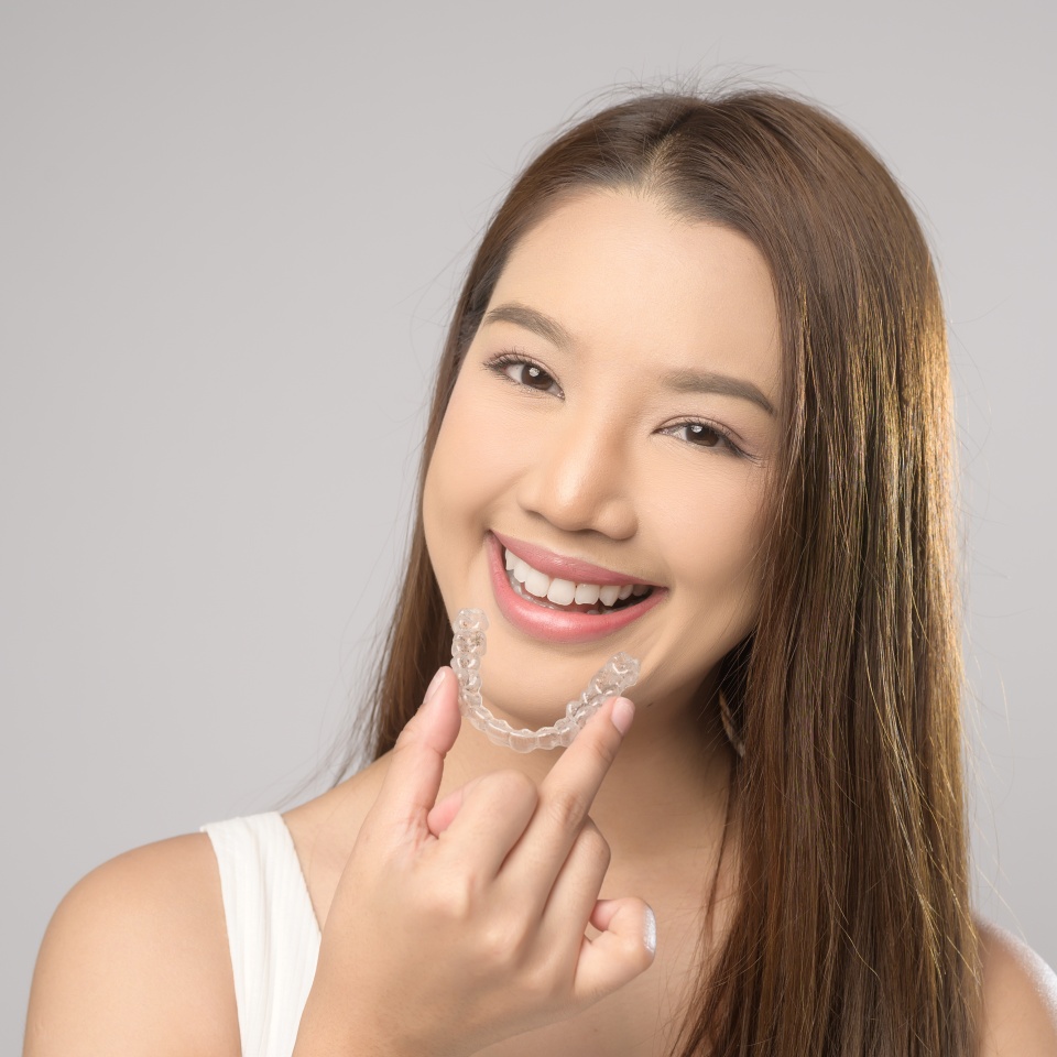 Una joven sonriente sosteniendo brackets Invisalign sobre fondo blanco de estudio, concepto de cuidado dental y ortodoncia.